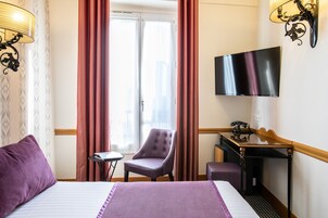 A hotel room with a bed, a chair, a desk, and a TV.