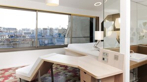 A modern hotel room with a large window, a desk, a bed, and a bathroom with a mirror and sink. - Hôtel Ducs D'Anjou (Paris)