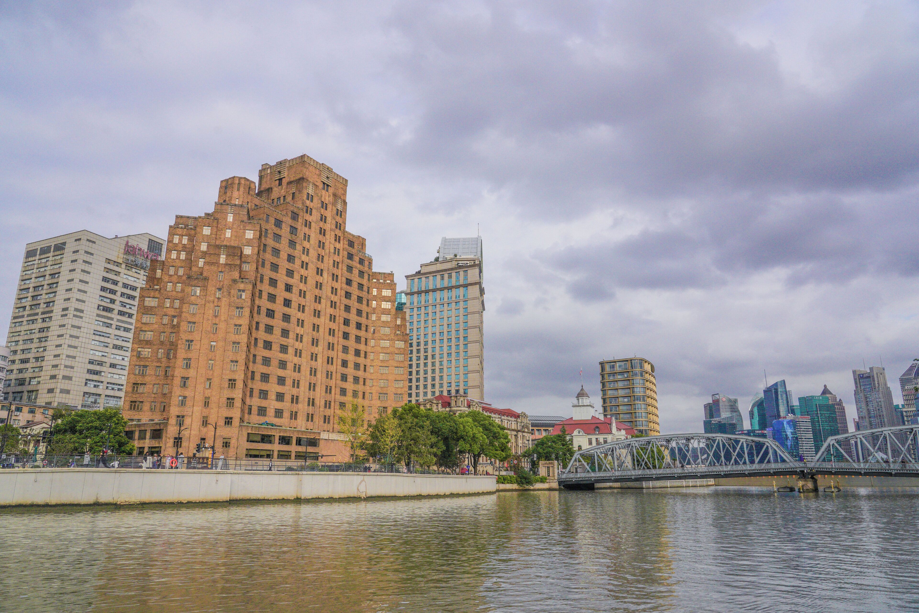 A cityscape with a prominent brown building, a modern glass structure, and a bridge over a river.