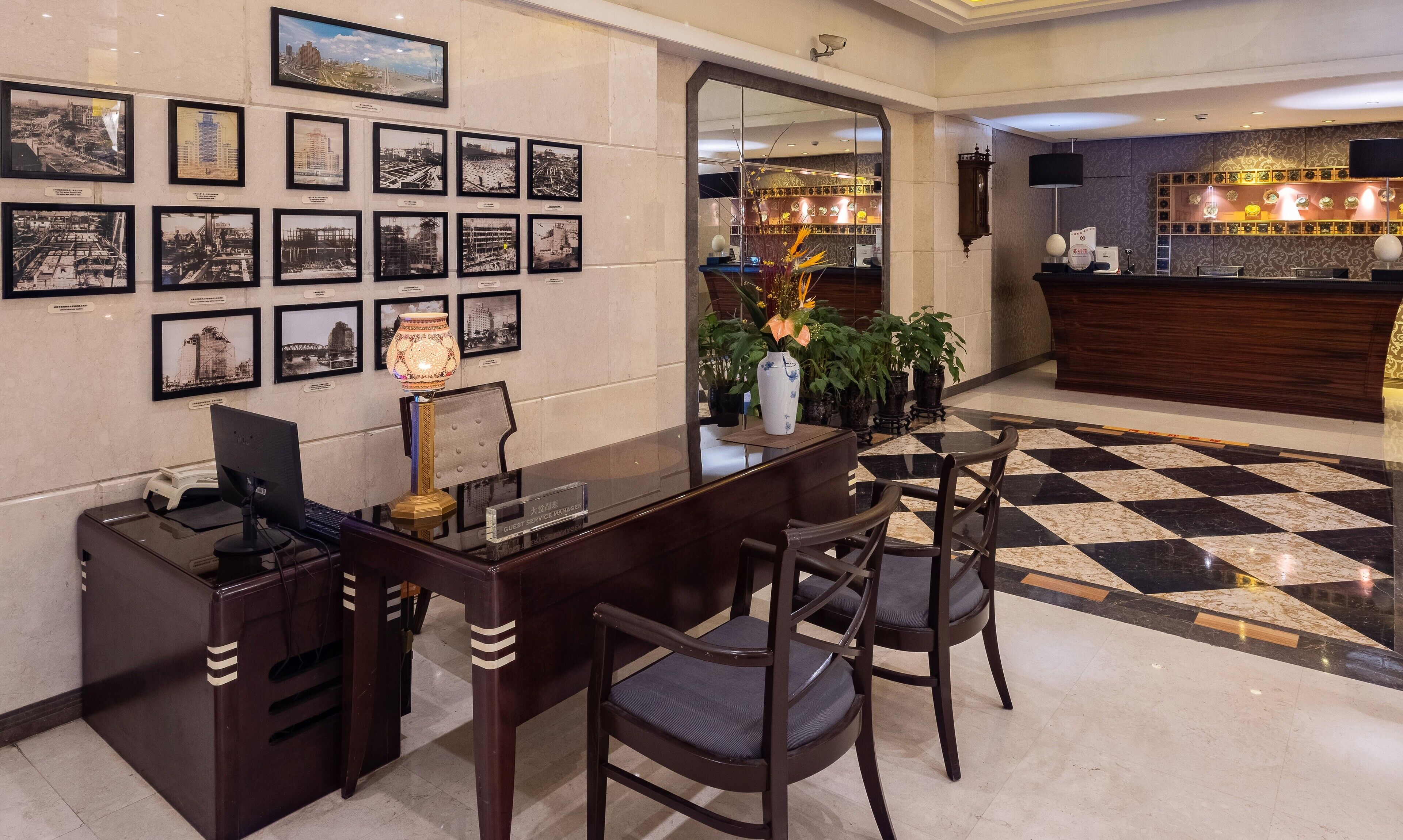Un hall d’hôtel avec un comptoir d’accueil, des tableaux encadrés accrochés au mur, un miroir et un sol à carreaux.