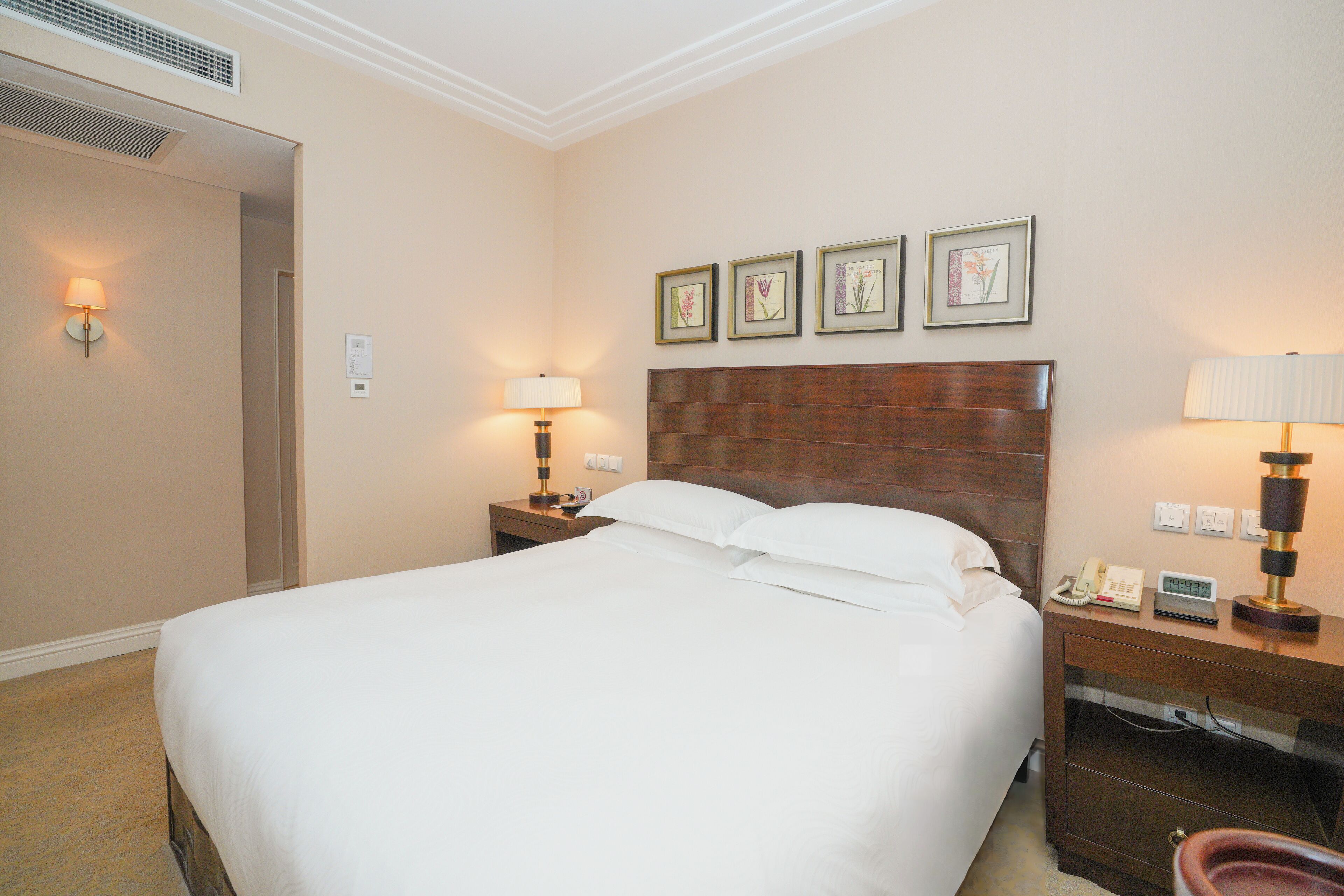 A hotel room with a large bed, two bedside tables with lamps, a wooden headboard, and three framed pictures on the wall.