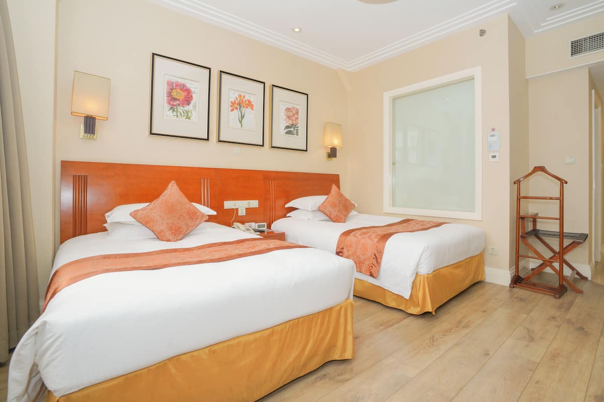 Quarto de hotel com duas camas, cabeceira de madeira, uma janela grande e arte floral emoldurada na parede.