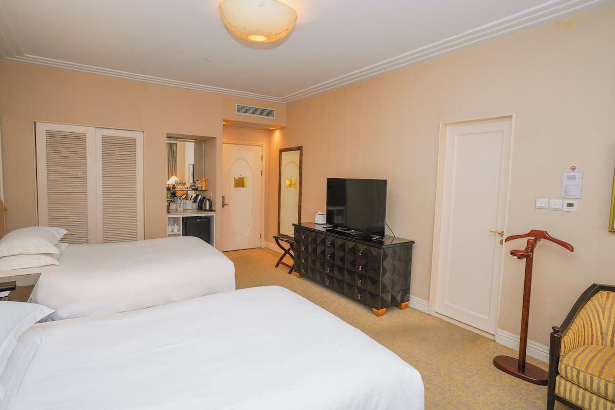 Quarto de hotel com duas camas, televisão, cômoda e uma cadeira.