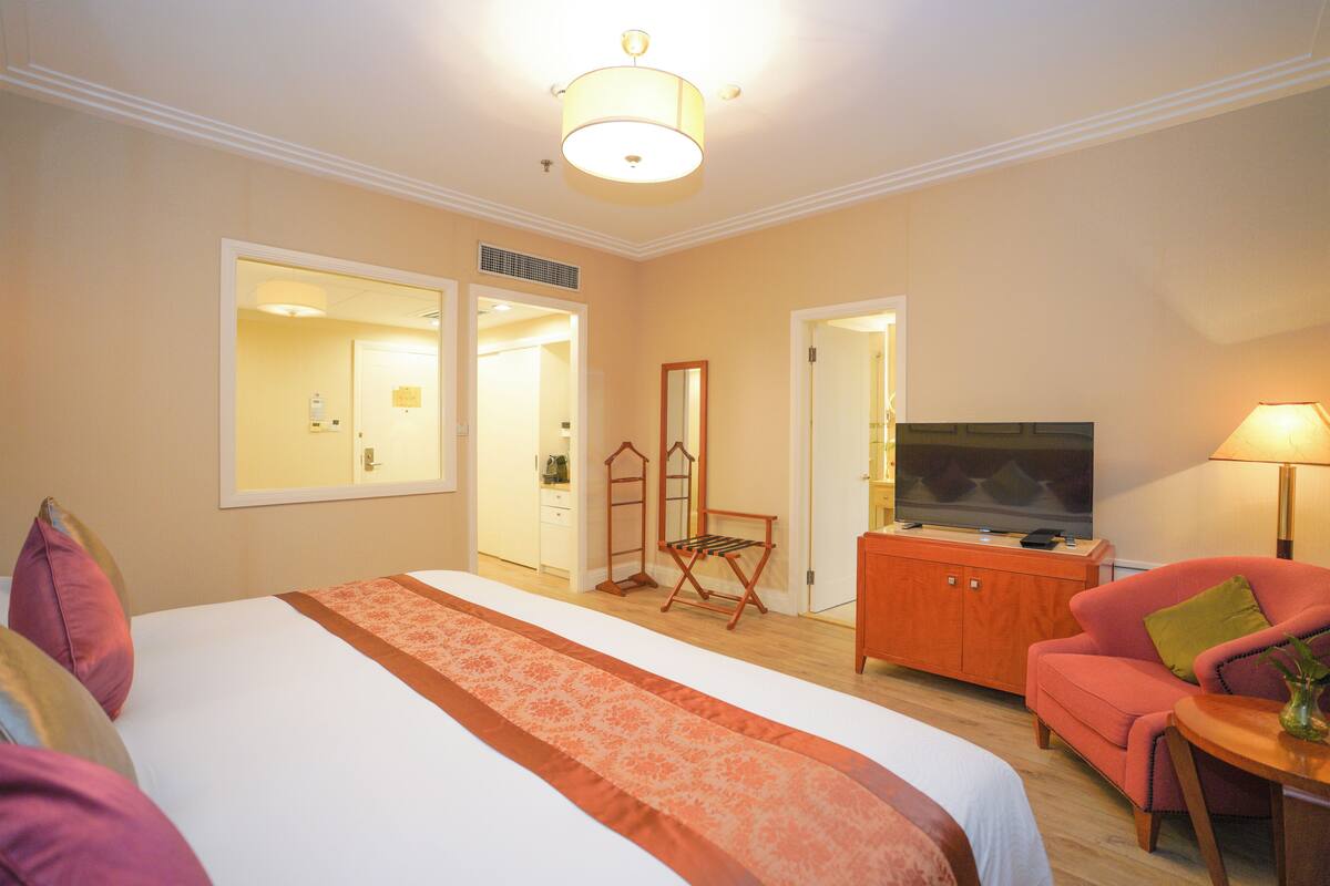 Quarto de hotel com uma cama grande, televisão, sofá e uma mesa pequena.