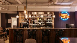 Zona de bar con un letrero de neón, taburetes y una barra con varias botellas.