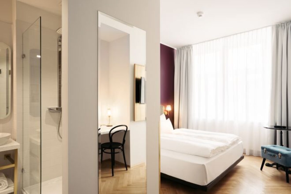 Une chambre d’hôtel comprenant un lit, un bureau, une chaise, un miroir et un espace douche.