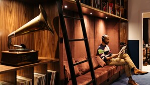 Un hombre sentado en un sofá en una habitación con paneles de madera, una estantería y un tocadiscos.