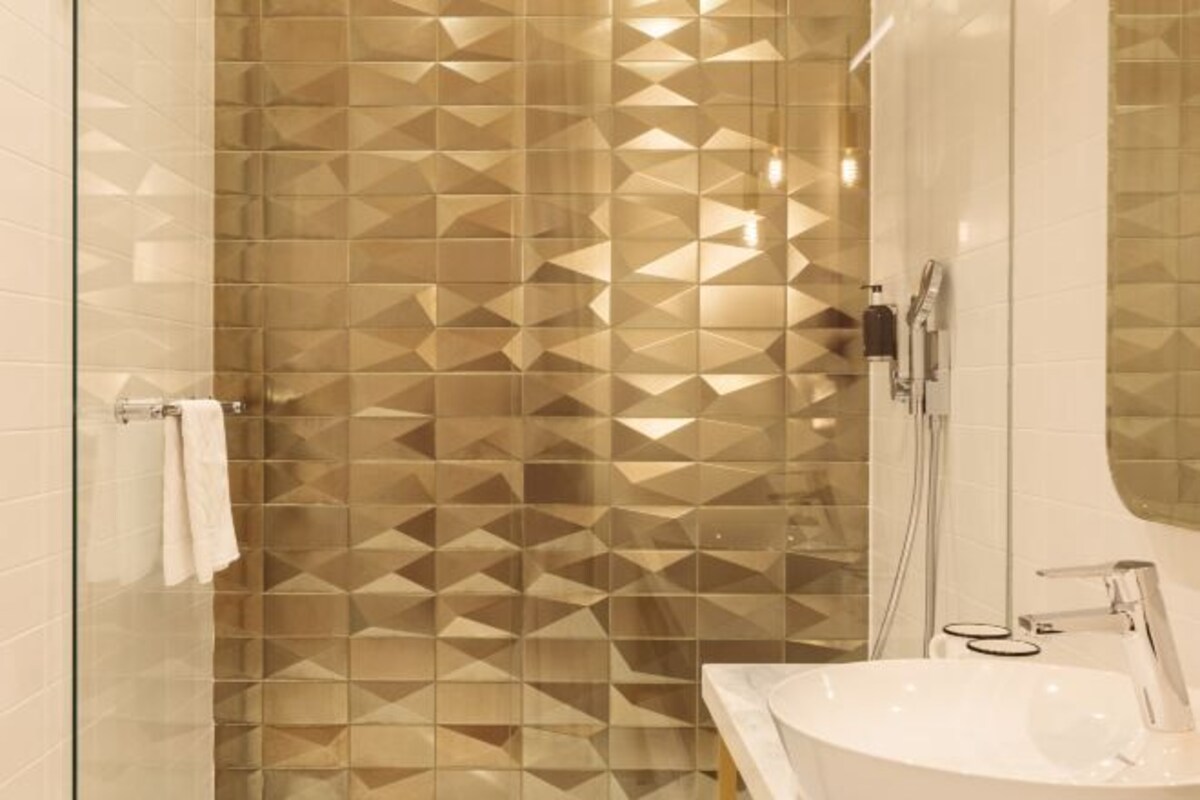 Une salle de bain moderne avec un mur de douche orné d’un motif géométrique, un lavabo blanc et un miroir.