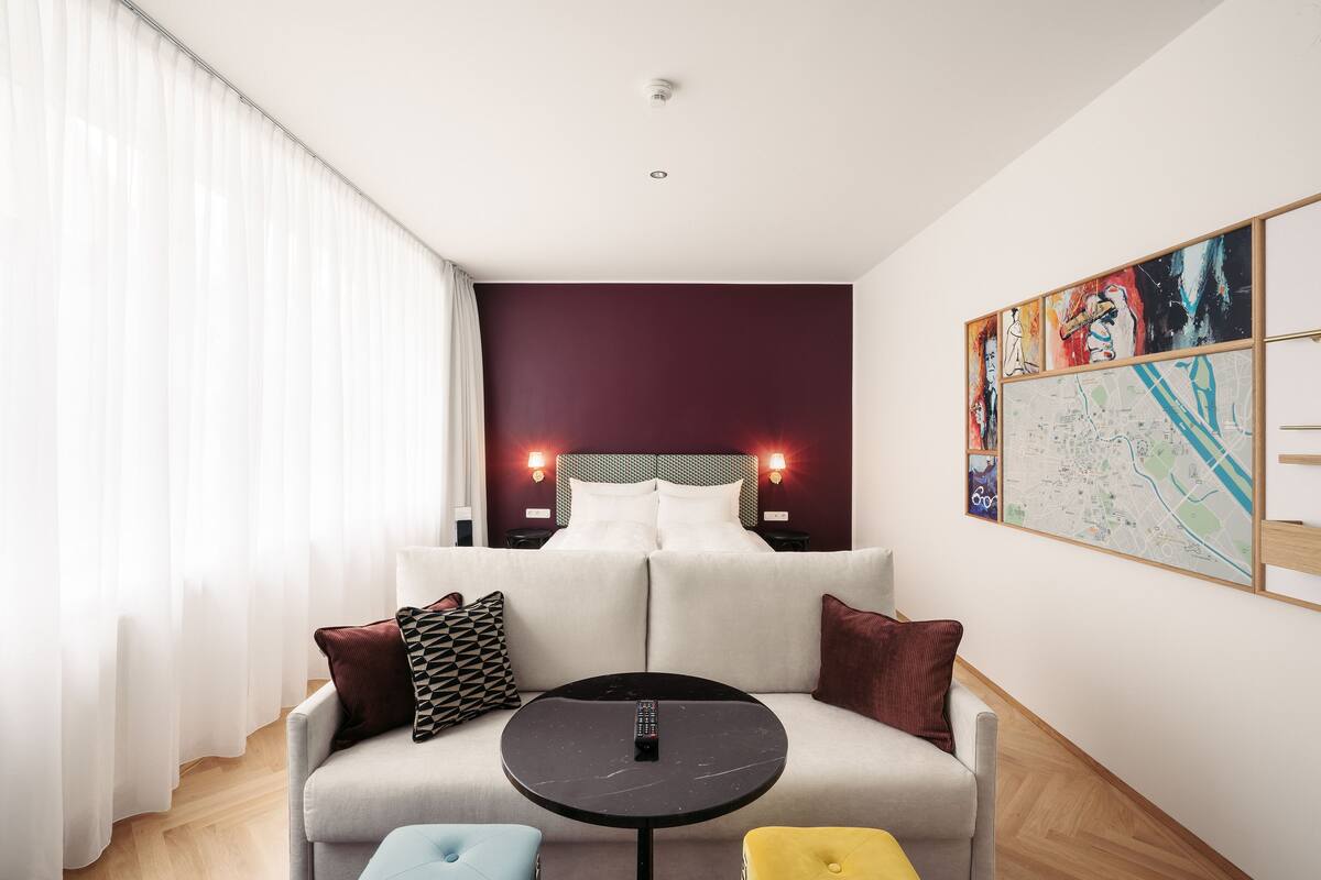 A modern hotel room with a large bed, a sofa, a small round table, and a map on the wall.