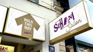 Señal de hotel con la leyenda 'Hotel Schani Salon' y una señal direccional que indica 'POR AQUÍ'.