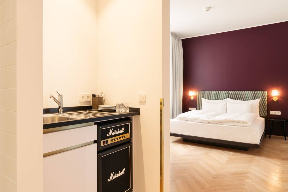 A modern hotel room with a bed, a small kitchenette with a sink, and a Marshall amplifier.