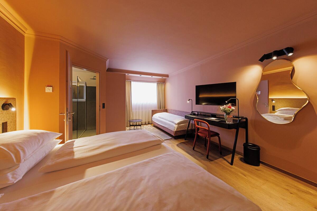 A hotel room with two beds, a desk with a chair, a TV, and a mirror.