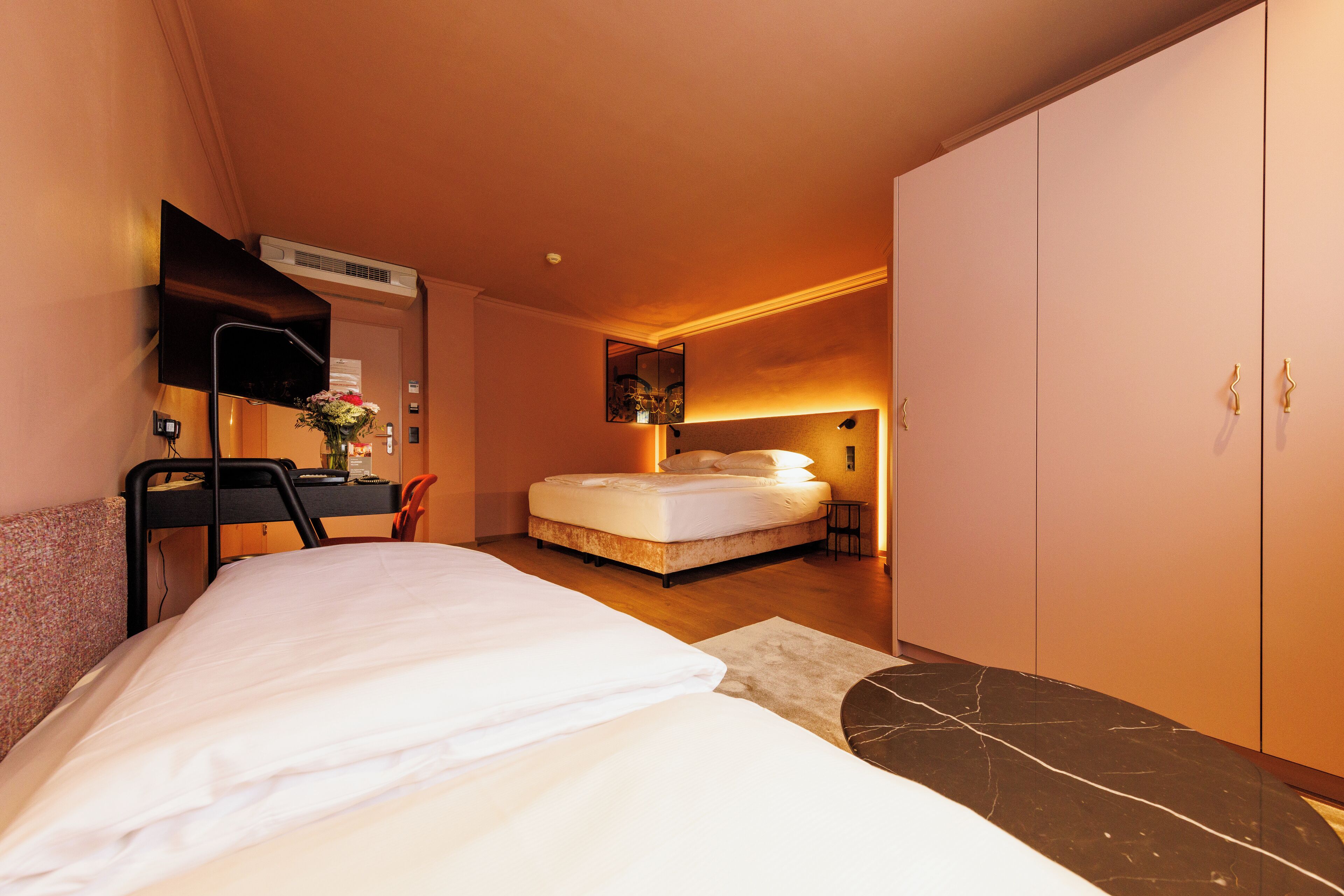 Un dormitorio con cama, escritorio, silla, armario y televisor en la pared.