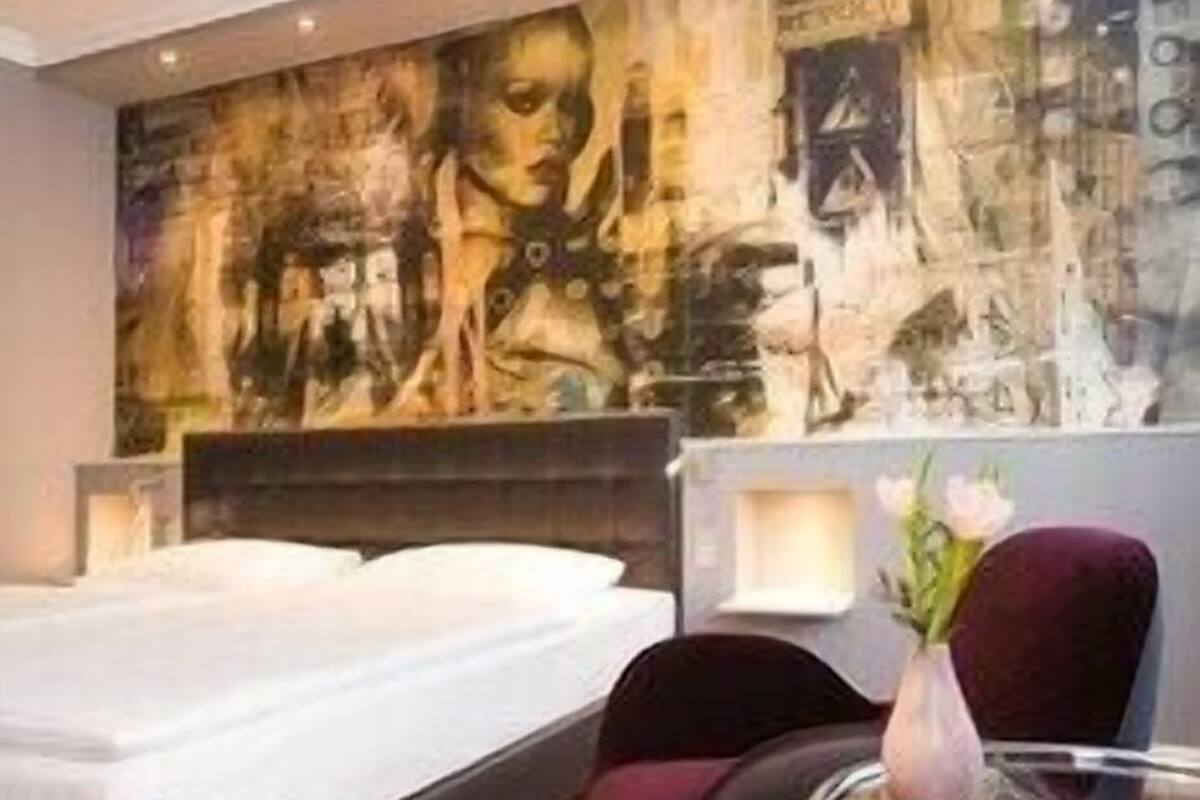 A modern hotel room with a large abstract mural, a glass table, and a comfortable bed.