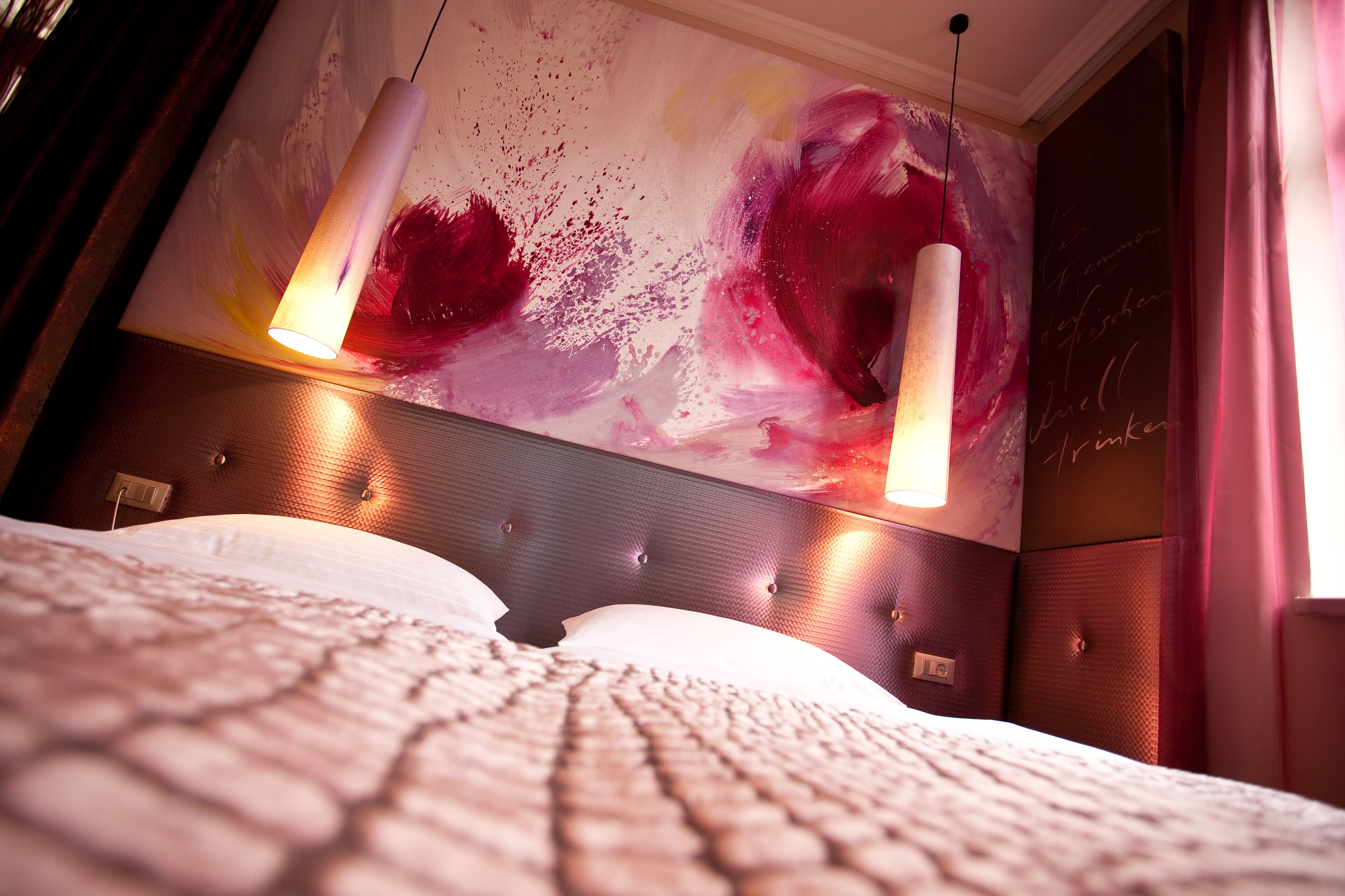 Quarto de hotel moderno com uma cama grande, cabeceira texturizada e um quadro abstrato vibrante na parede.