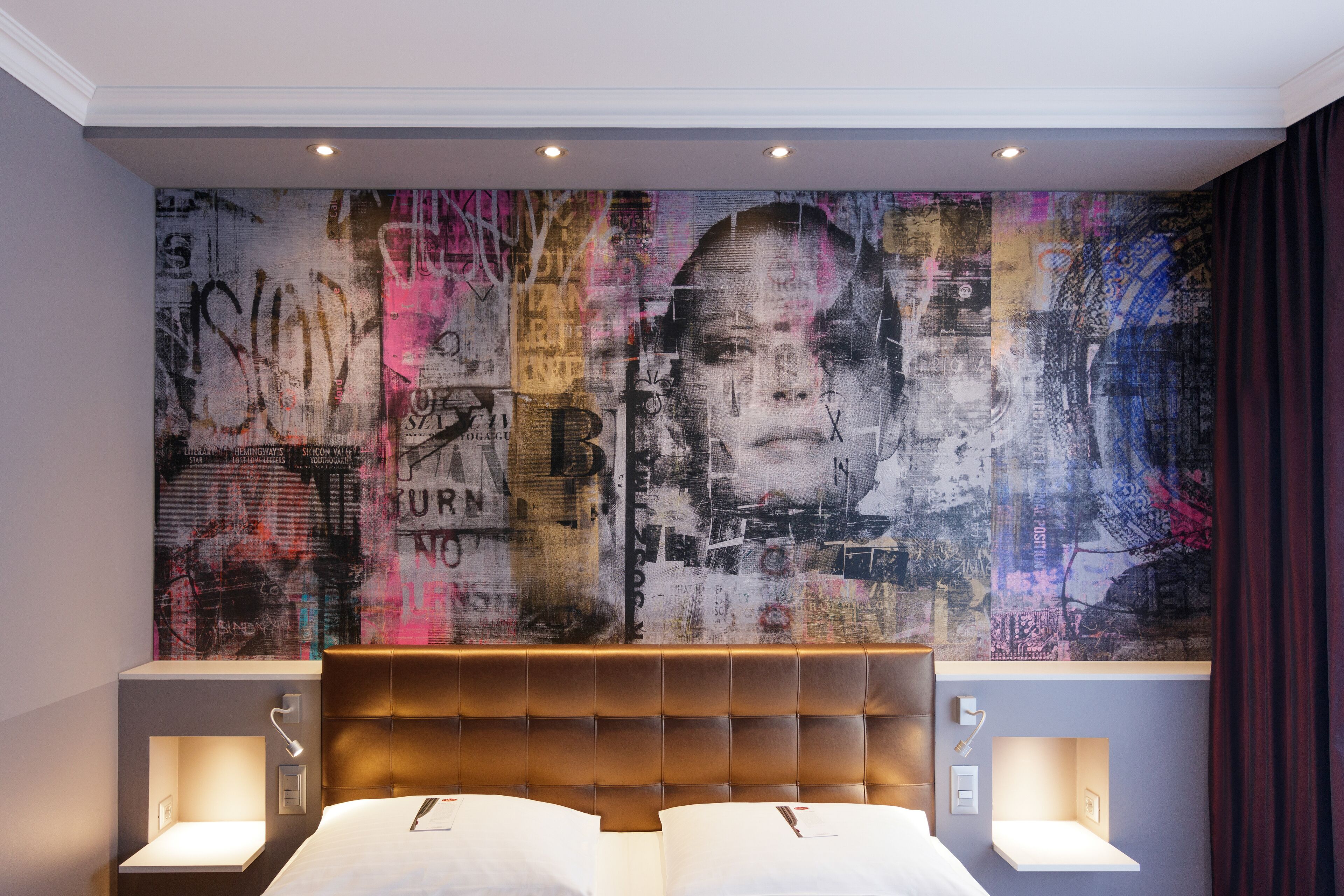 A hotel room with a large, colorful abstract mural on the wall, a tufted headboard, and bedside lamps.