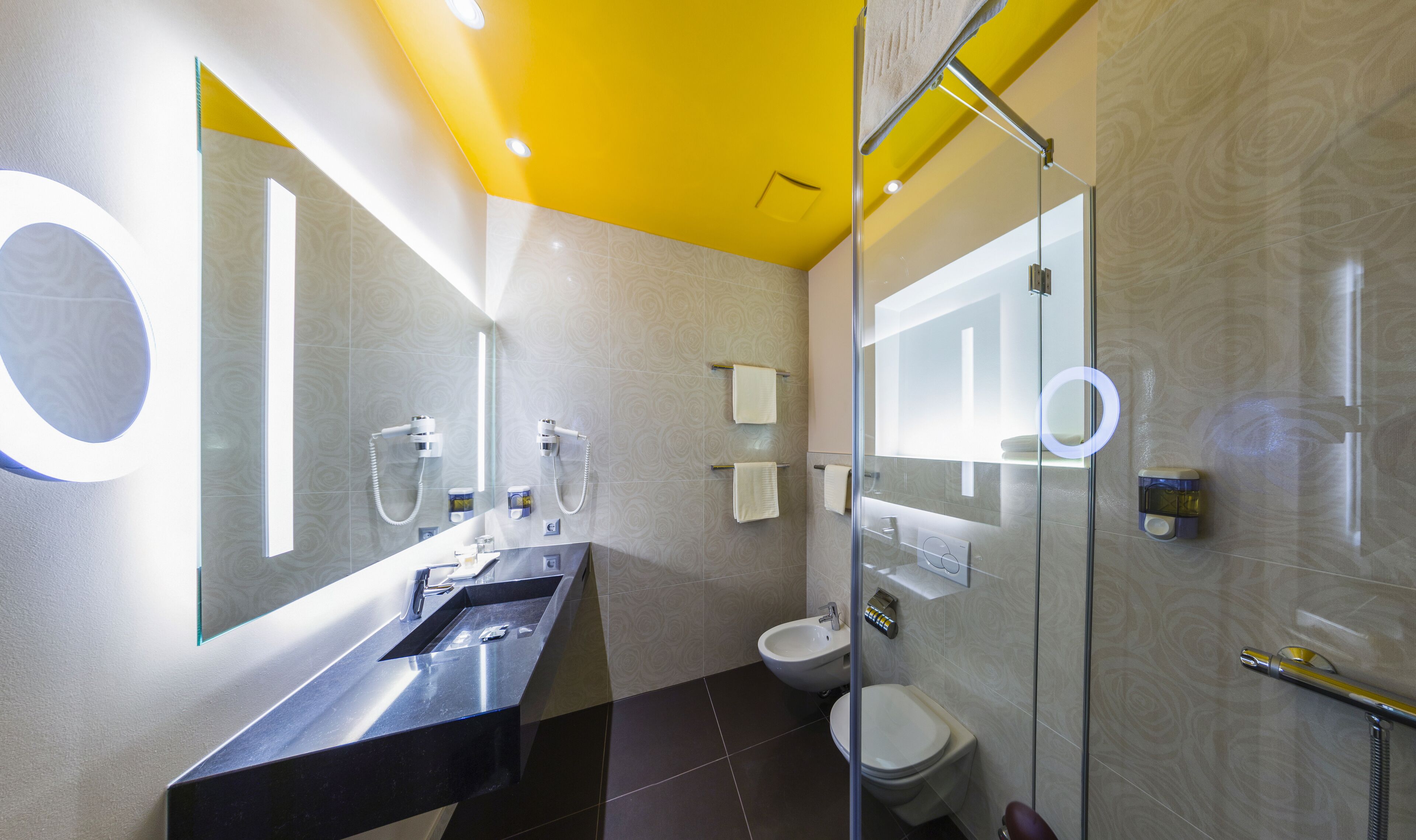 Un bany modern amb un mirall gran, un lavabo negre, un vàter i una zona de dutxa amb envàs de vidre.