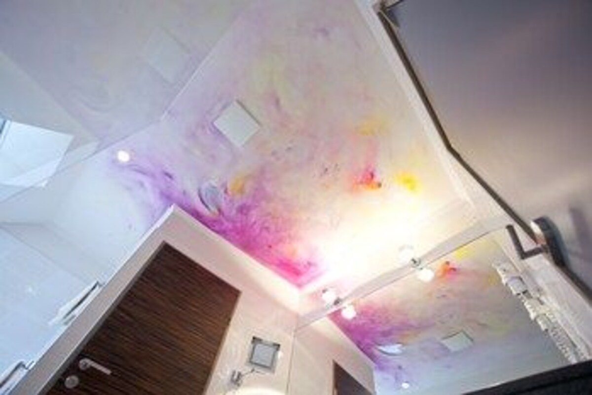 A bathroom with a large mirror, a wooden vanity, and a ceiling with a unique light fixture.