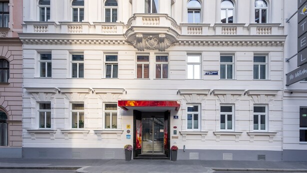 A multi-story building with a classical architectural style, featuring a central entrance with a red awning, multiple windows, and a flat roof. - Der Wilhelmshof (Vienna)