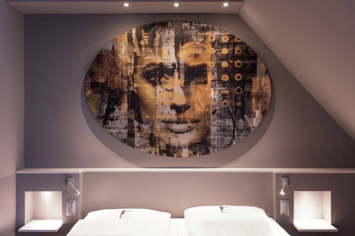 A bedroom with a circular artwork on the wall, two bedside tables with lamps, and a bed with white linens.