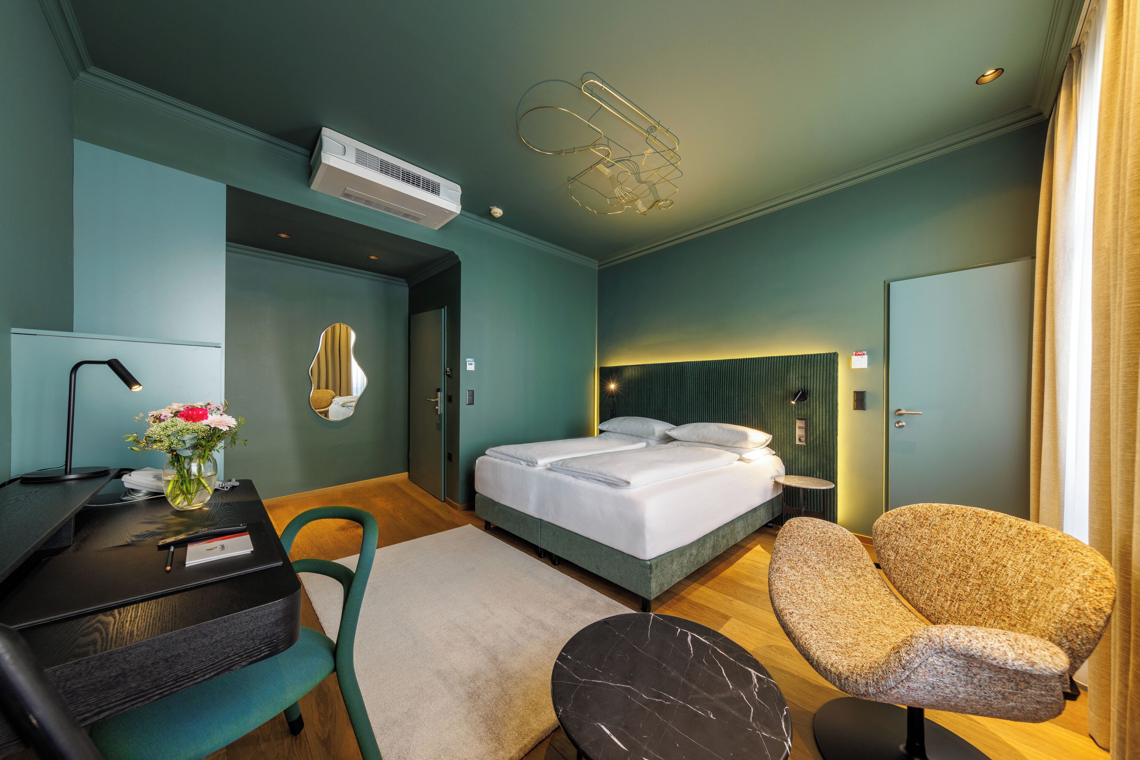 A modern hotel room with a bed, a desk, a chair, and a small table.