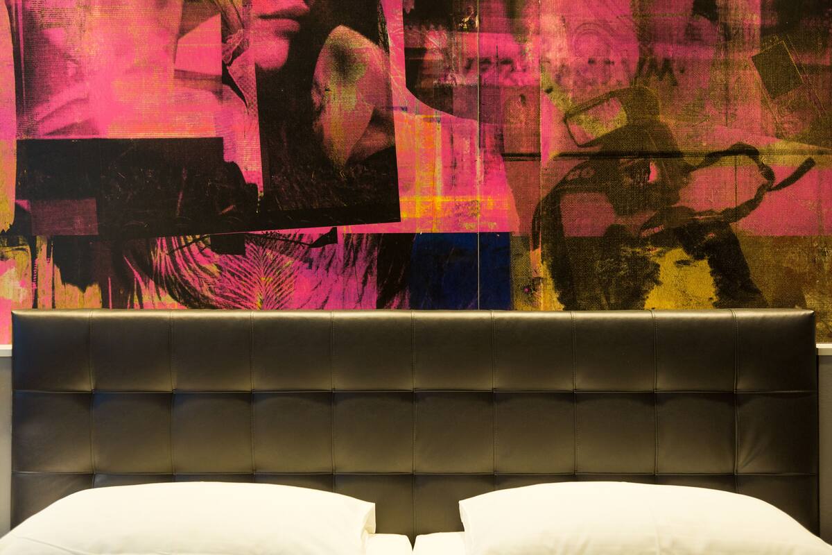 A bed with a tufted headboard and white pillows, set against a wall with a colorful abstract painting.