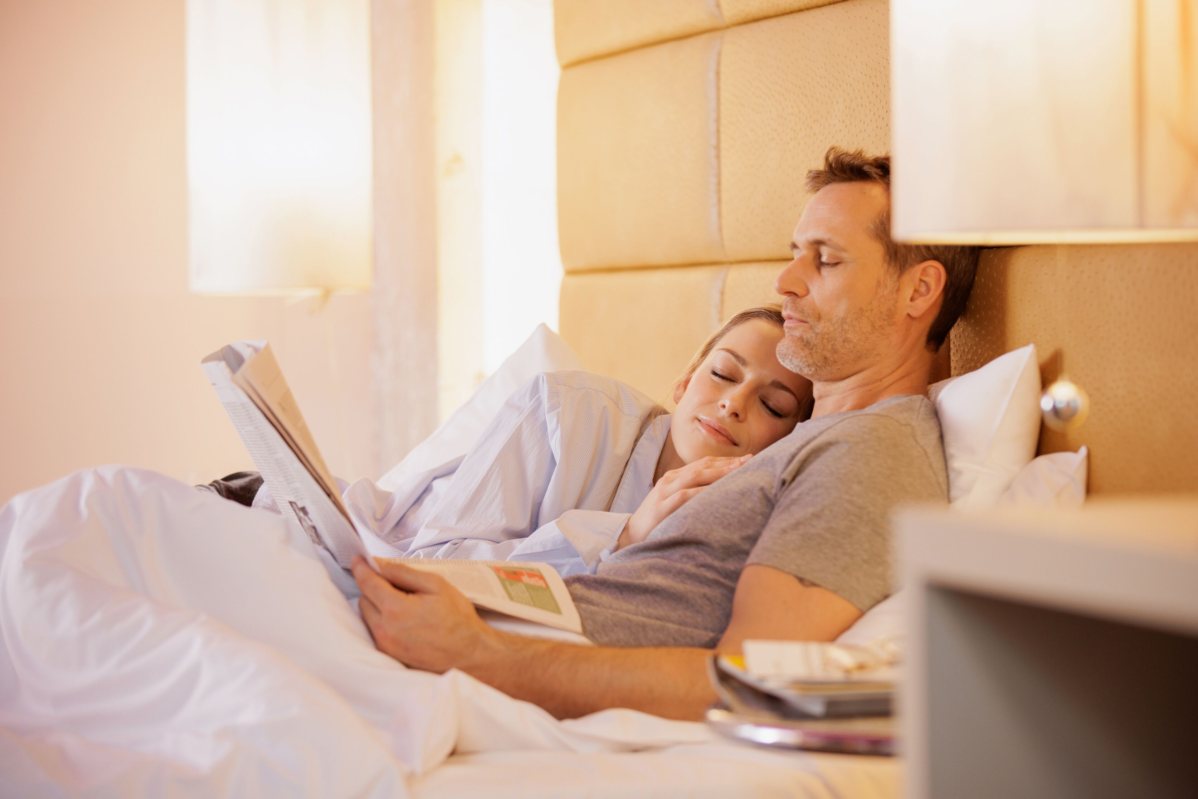 Una pareja acostada en la cama leyendo un libro.
