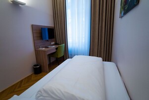 Quarto de hotel com cama, escrivaninha, cadeira, televisão e janela com cortinas.