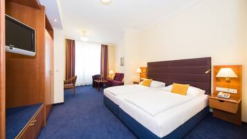 A hotel room with a large bed, a desk, a chair, a television, and a lamp.
