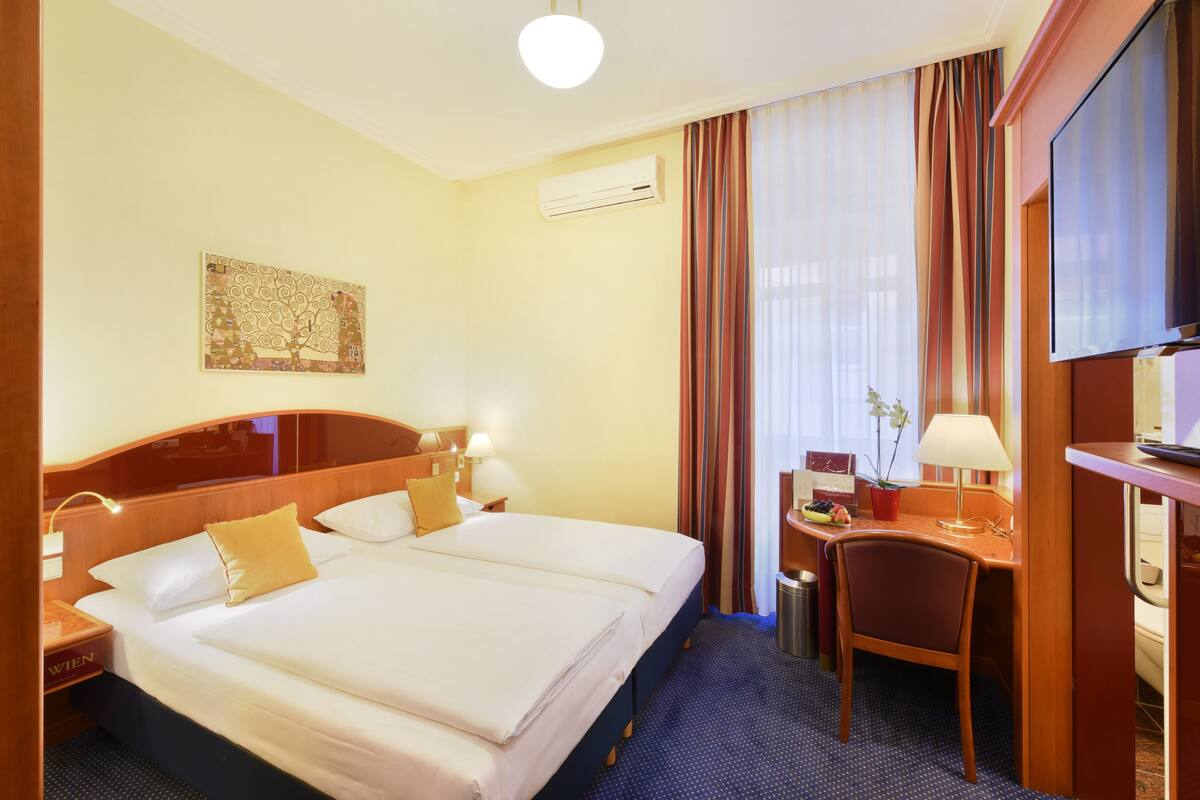 A hotel room with a double bed, a desk with a chair, an air conditioning unit, and a television.