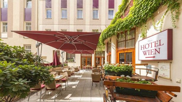 An outdoor patio with tables and chairs, a large umbrella, and a sign for Hotel Wien. - Austria Classic Hotel Wien (Vienna)