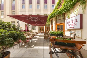 An outdoor patio with tables and chairs, a large umbrella, and a sign for Hotel Wien. - Austria Classic Hotel Wien (Vienna)
