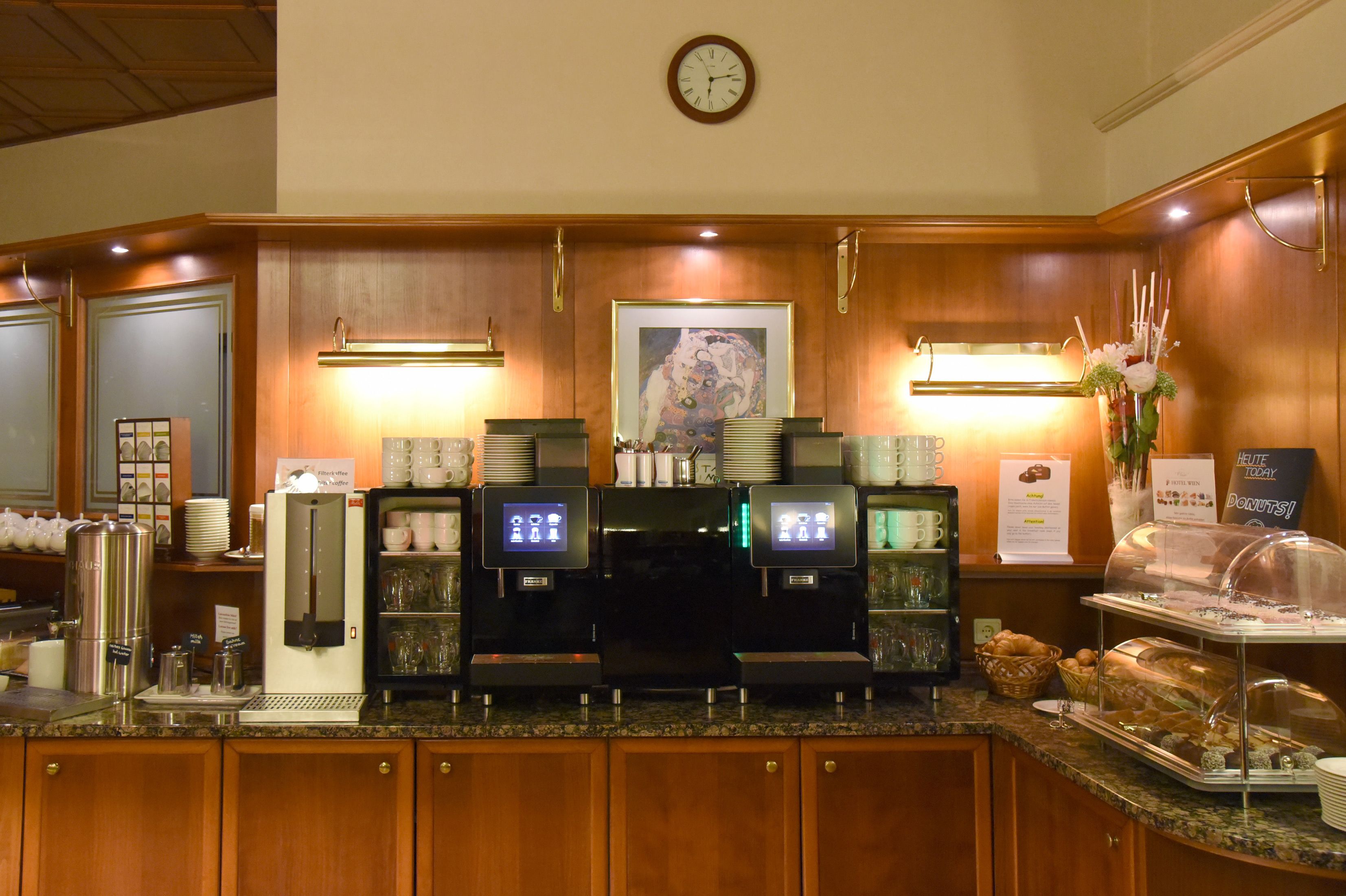 Zona de desayuno de hotel con una máquina de café, estación de té y una variedad de pasteles.