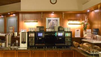 Zona de desayuno de hotel con una máquina de café, estación de té y una variedad de pasteles.