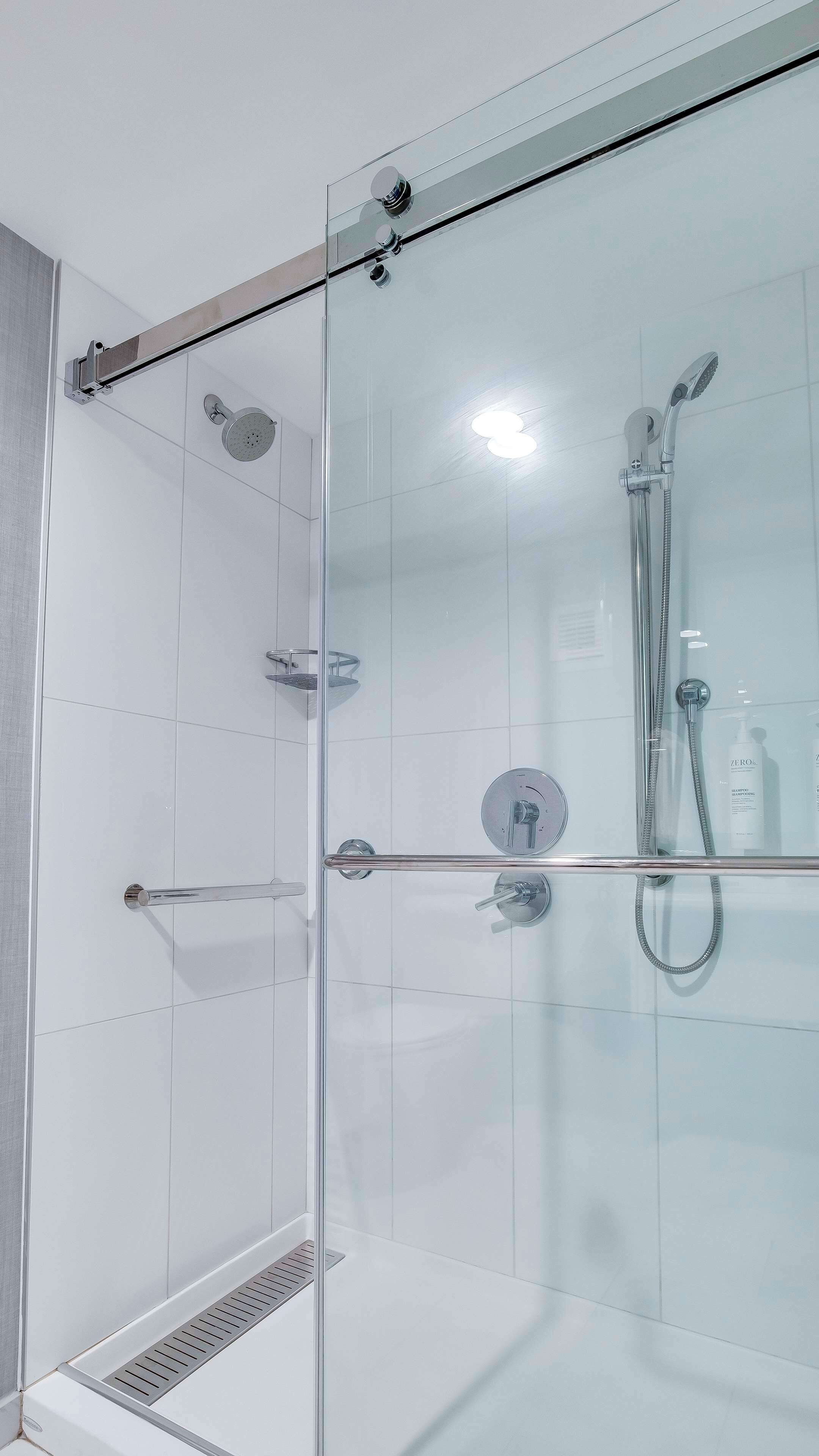 Une cabine de douche moderne dotée d’une porte en verre, d’un pommeau de douche à main, d’un robinet mural et d’un autre pommeau de douche à main.