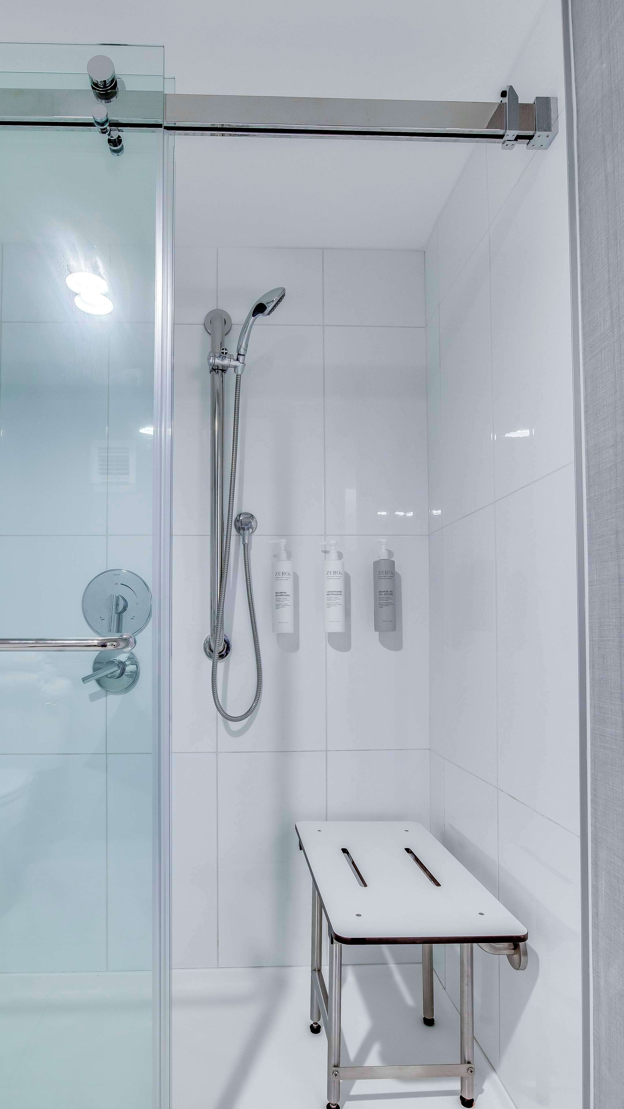 A modern bathroom with a glass shower enclosure, a handheld showerhead, a handheld shower attachment, and a small table with a towel.