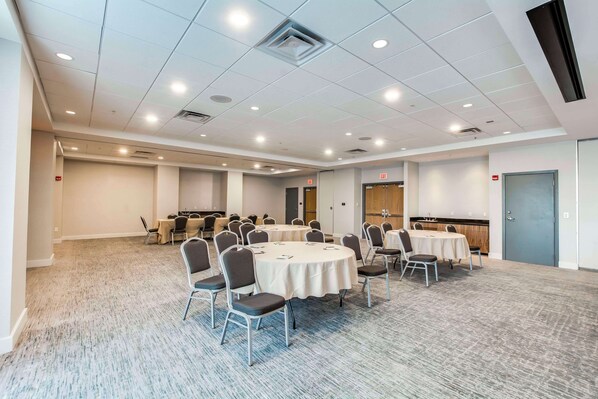 A conference room with round tables and chairs, carpeted flooring, and recessed lighting.