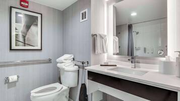 Ein modernes Badezimmer mit Toilette, Waschbecken und Dusche. An der Wand hängt ein gerahmtes Bild, ein Rauchmelder ist angebracht und es gibt einen Handtuchhalter.