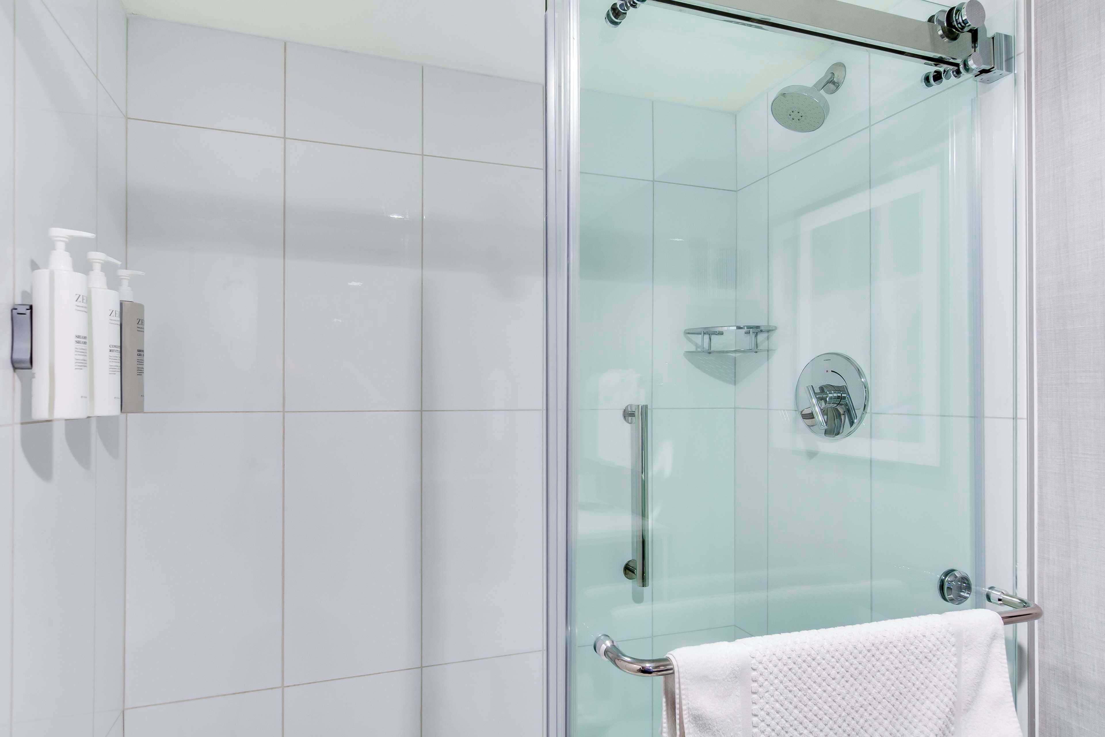 A modern bathroom with a glass-enclosed shower, white tiles, and a towel rack.