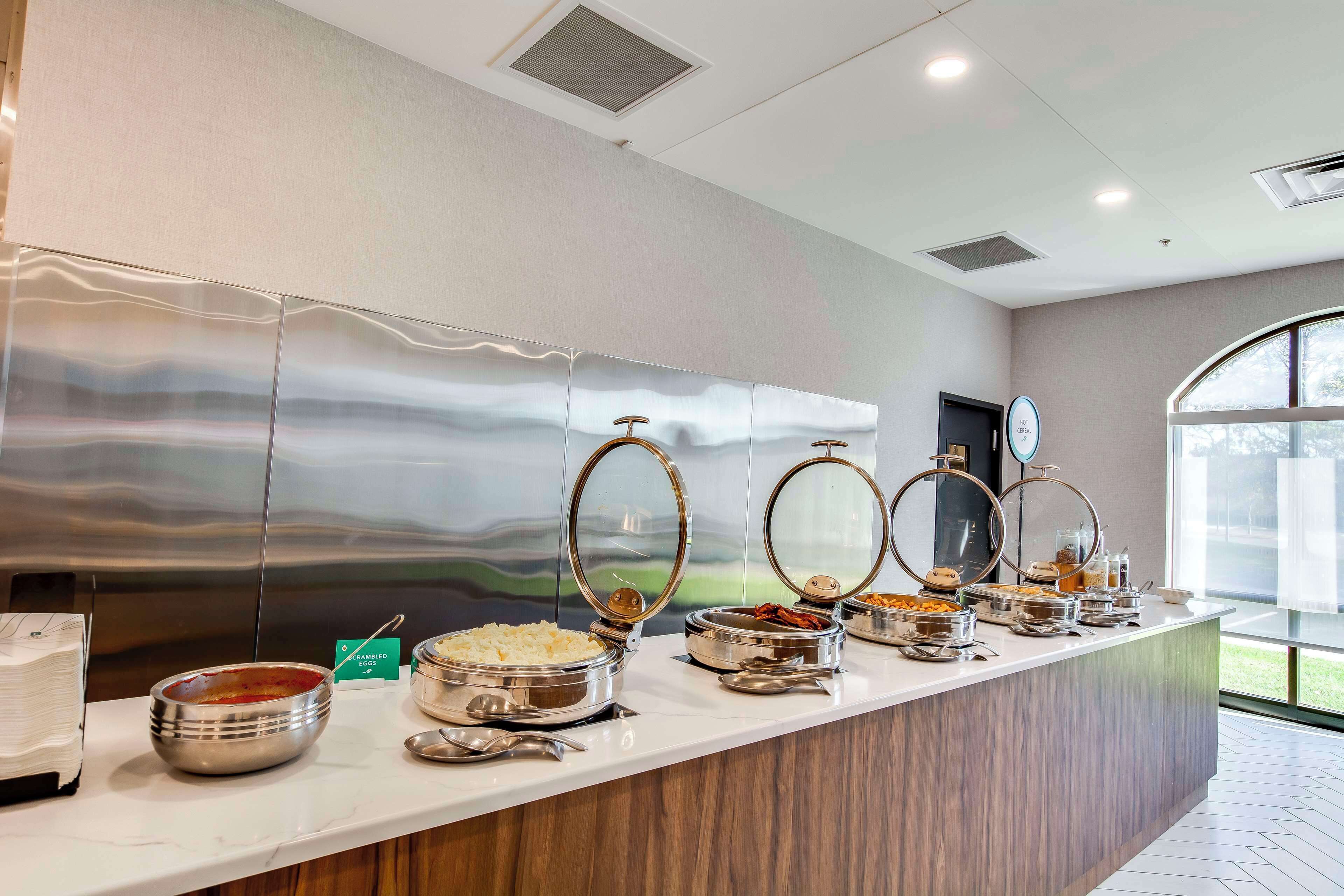 Mesa de buffet con distintos alimentos y un electrodoméstico de acero inoxidable grande al fondo.