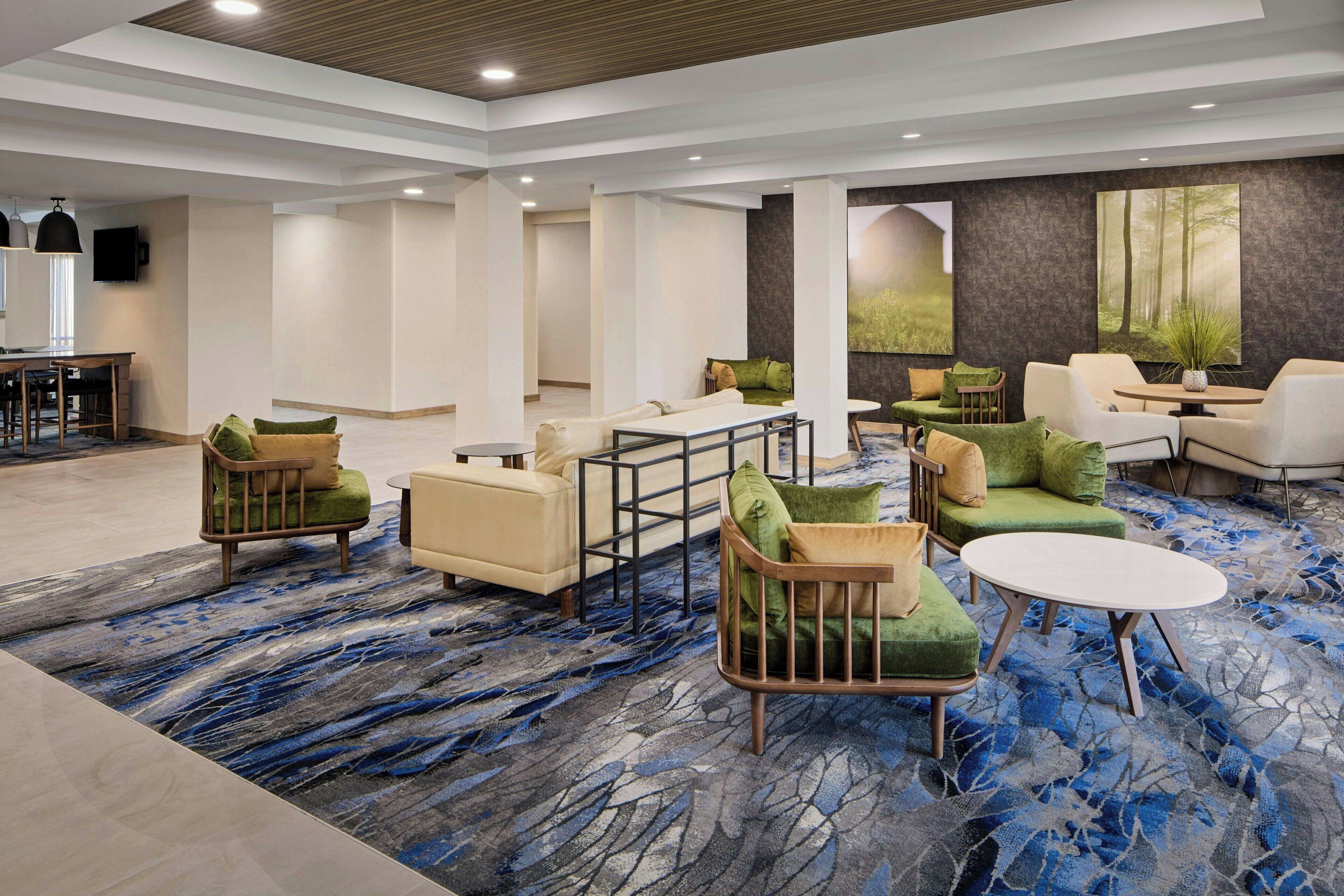 A spacious lobby with modern furniture, a marble-patterned carpet, and a large painting of a forest.