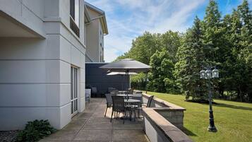Een terras buiten met een tafel, stoelen, een grote parasol en een lantaarn.