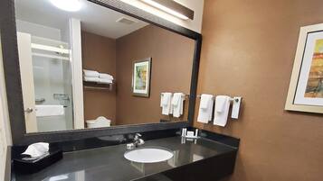 Une salle de bain moderne avec un grand miroir, un plan de toilette noir, un lavabo blanc et un porte-serviettes avec des serviettes blanches.