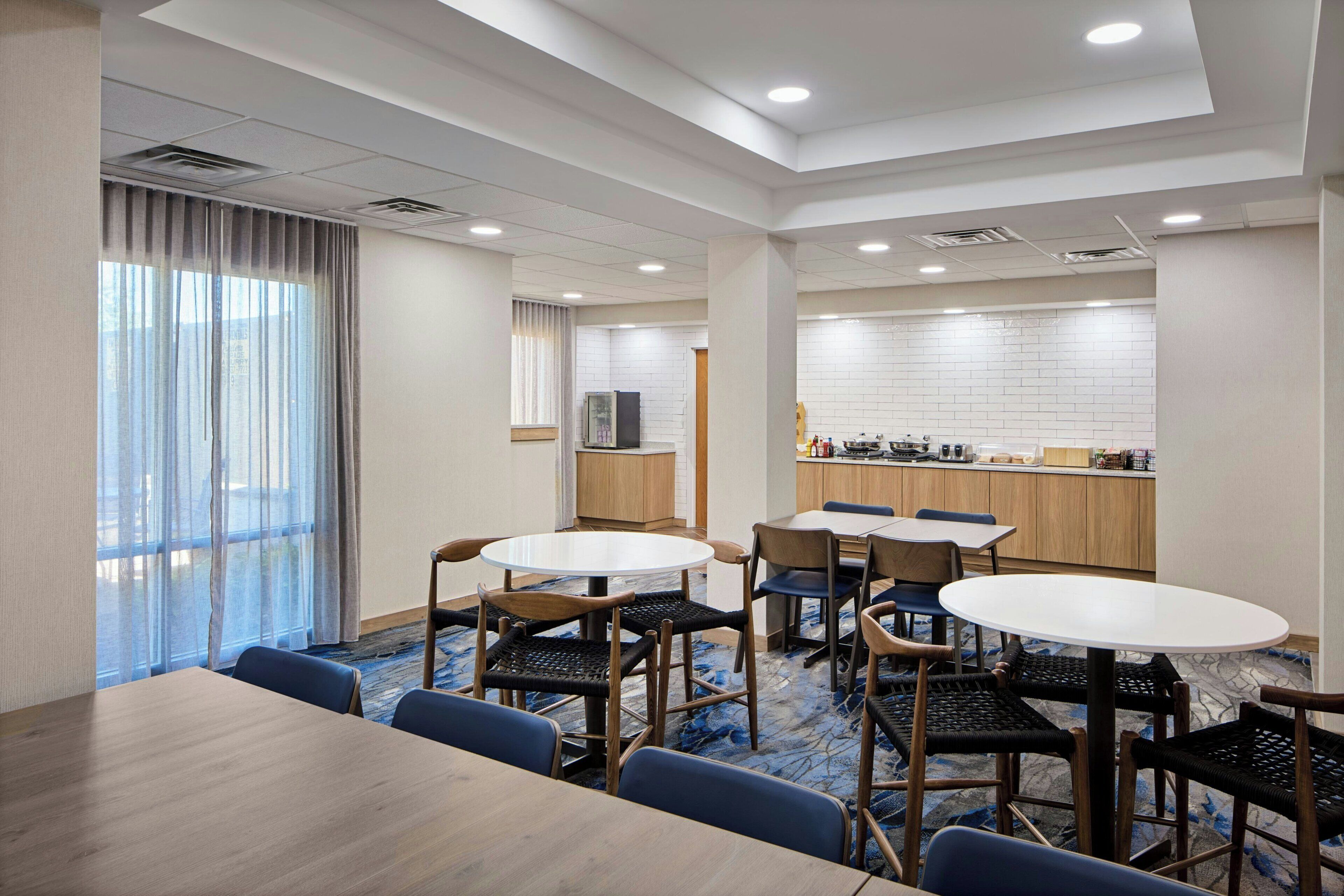 Habitación de hotel con comedor, cocina y un amplio ventanal con cortinas.