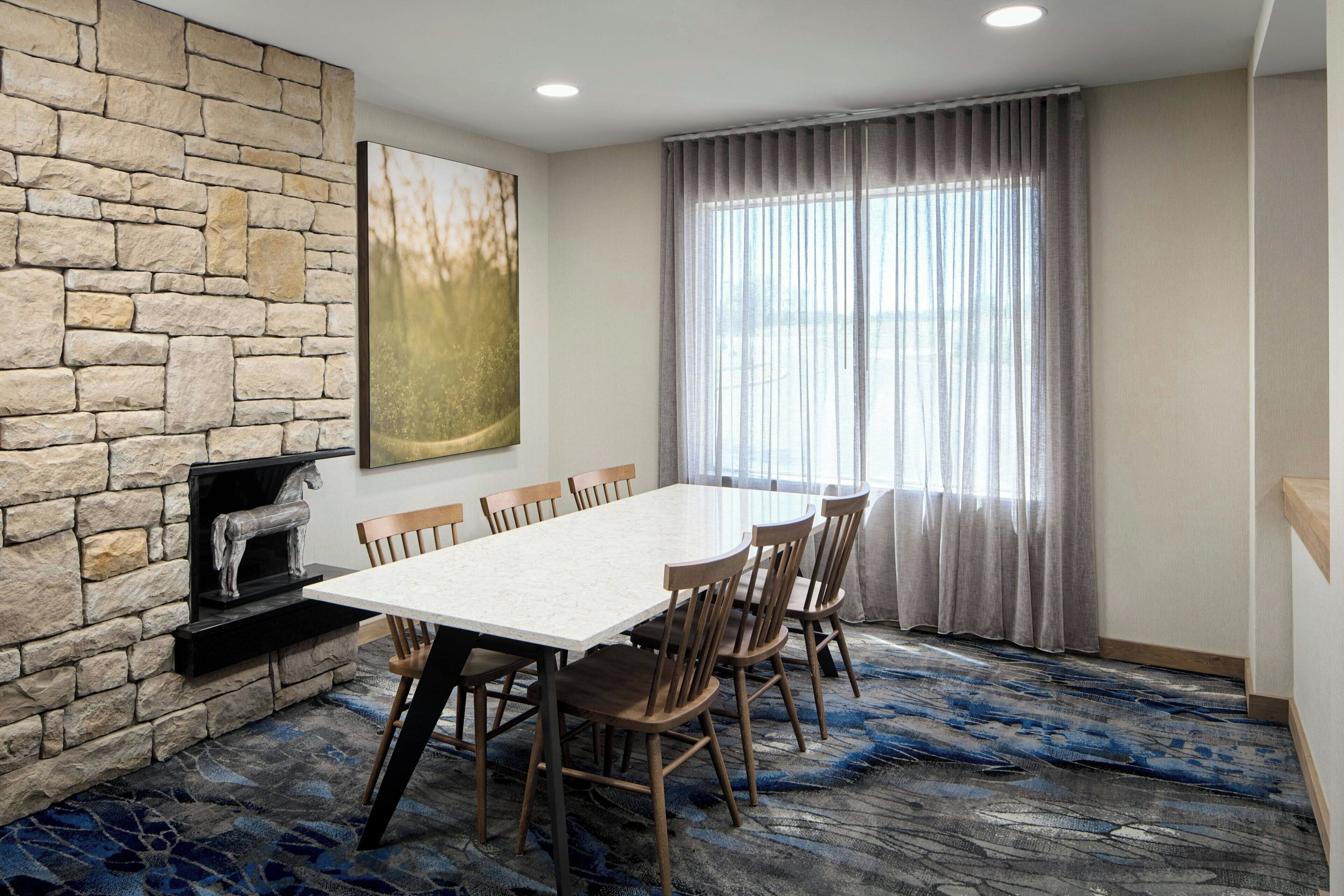 A conference room with a stone wall, a large painting, a fireplace, and a view through a window with curtains.
