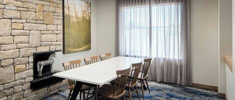 A conference room with a stone wall, a large painting, a fireplace, and a view through a window with curtains.