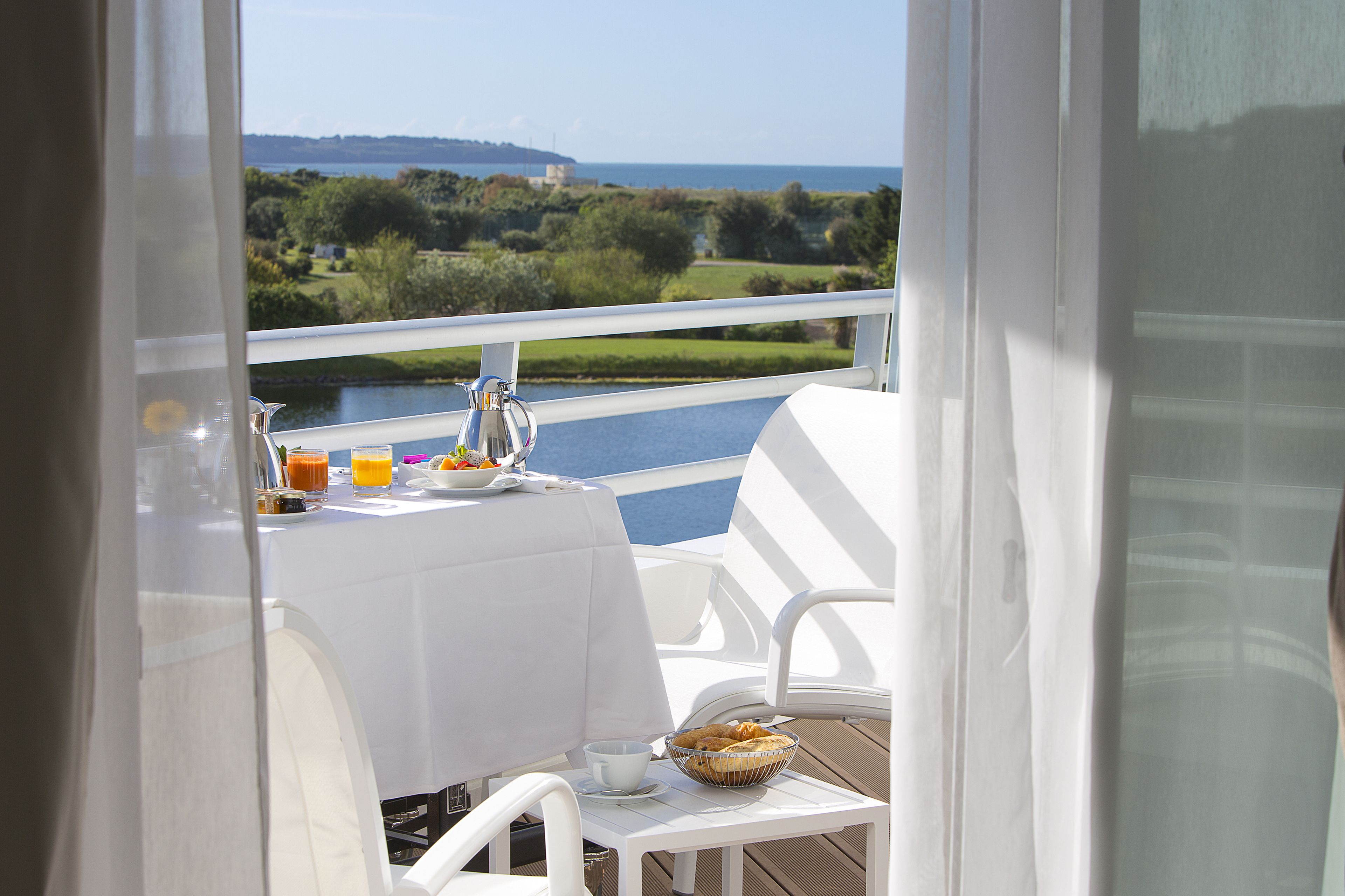 Un balcon avec une table préparée pour le petit-déjeuner, donnant sur une étendue d’eau et une végétation luxuriante.