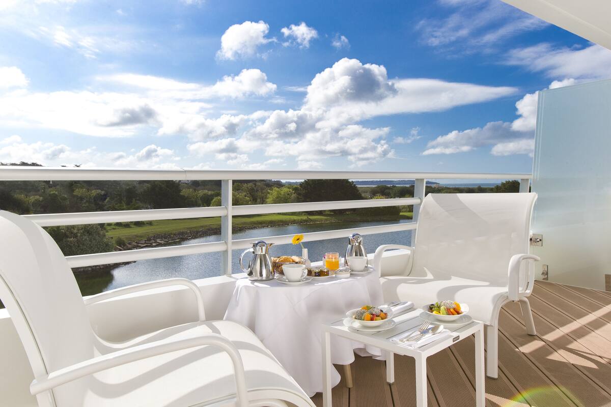 A balcony with a table set for breakfast, overlooking a river and greenery.