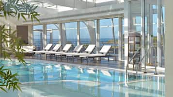 Relax by the ocean-view pool, surrounded by lounge chairs and glass walls.