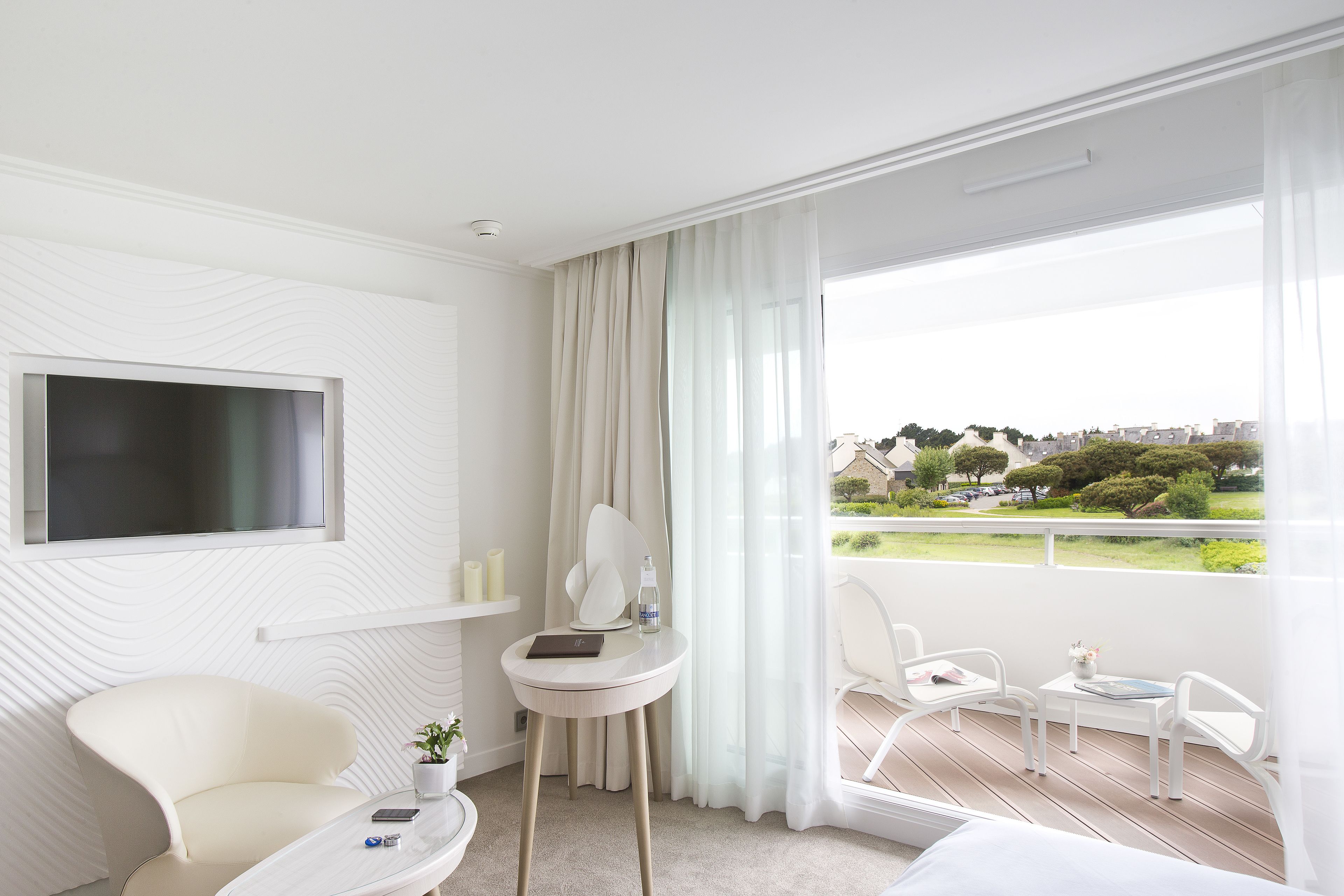 Habitación de hotel moderna con balcón, televisión de pantalla plana, una pequeña mesa redonda con una planta y una silla.